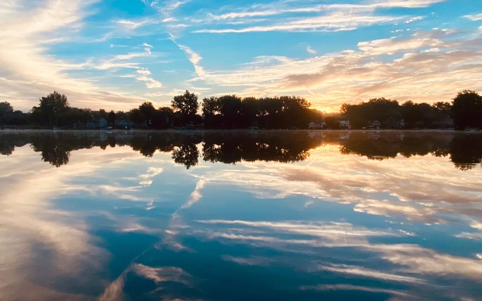 Sunrise on Lake Bella Vista, with trees and lakeside homes in silhouette and the clouds and golden light mirrored in still water.