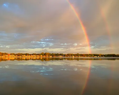 A rainbow arcs over Silver Lake, with lakefront homes along the far shore and the whole scene mirrored in calm water.