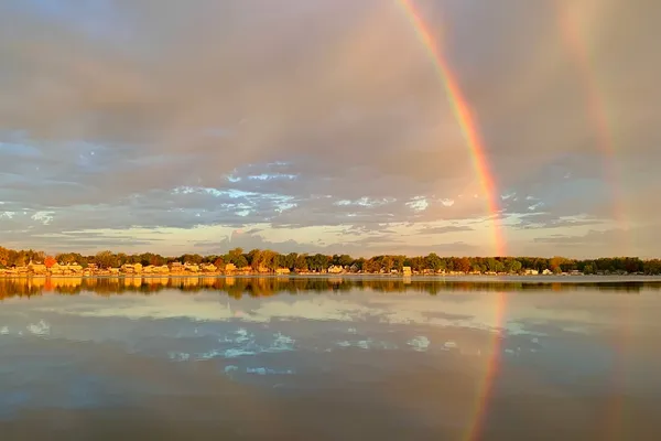 A rainbow arcs over Silver Lake, with lakefront homes along the far shore and the whole scene mirrored in calm water.